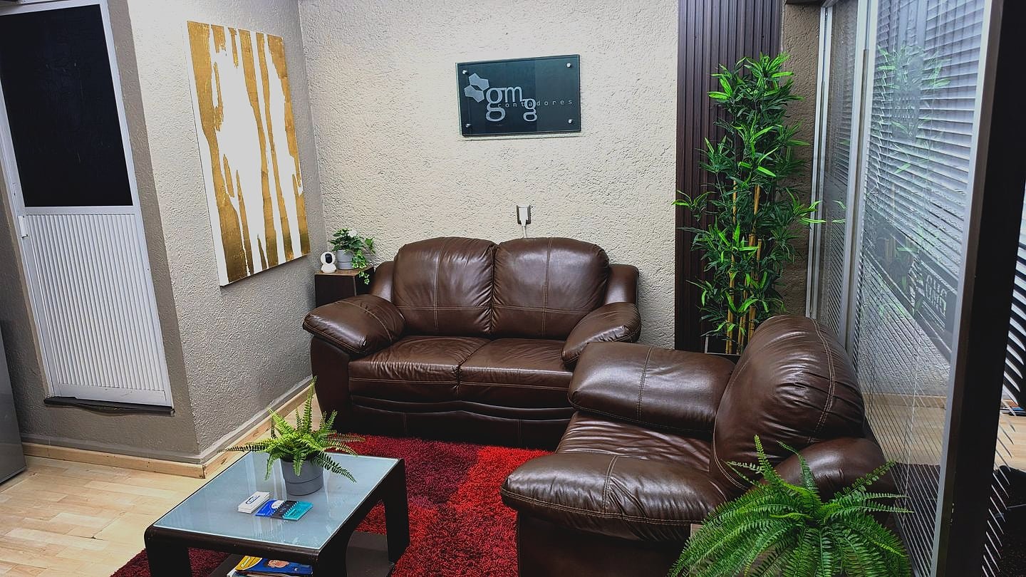 Sala de espera de GMG Contadores: la placa del despacho en el muro, sillones de piel, mesa de centro y tapete